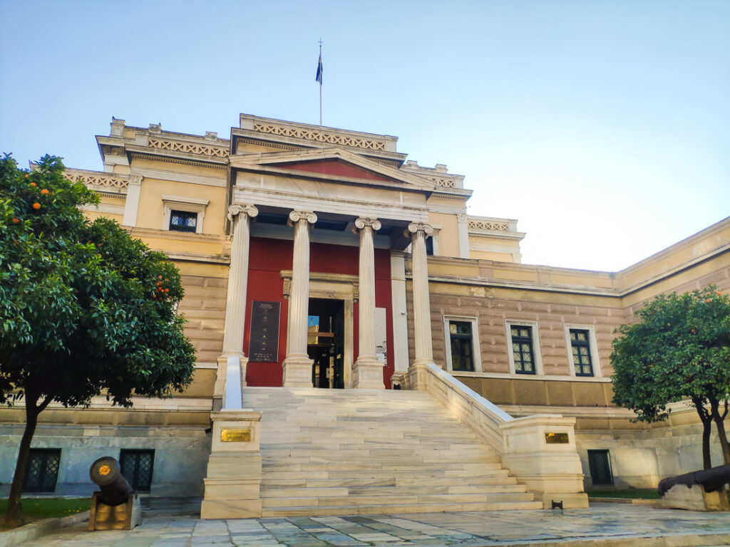 An image of the main entrance to the National Historical Museum at the neoclassical Old Parliament House in Athens, Greece.  The portico and its supporting pillars are built in the Ionic Order.