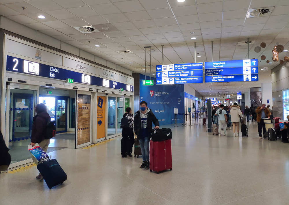 The Athens airport arrivals corridor with blue coloured signage with white text.